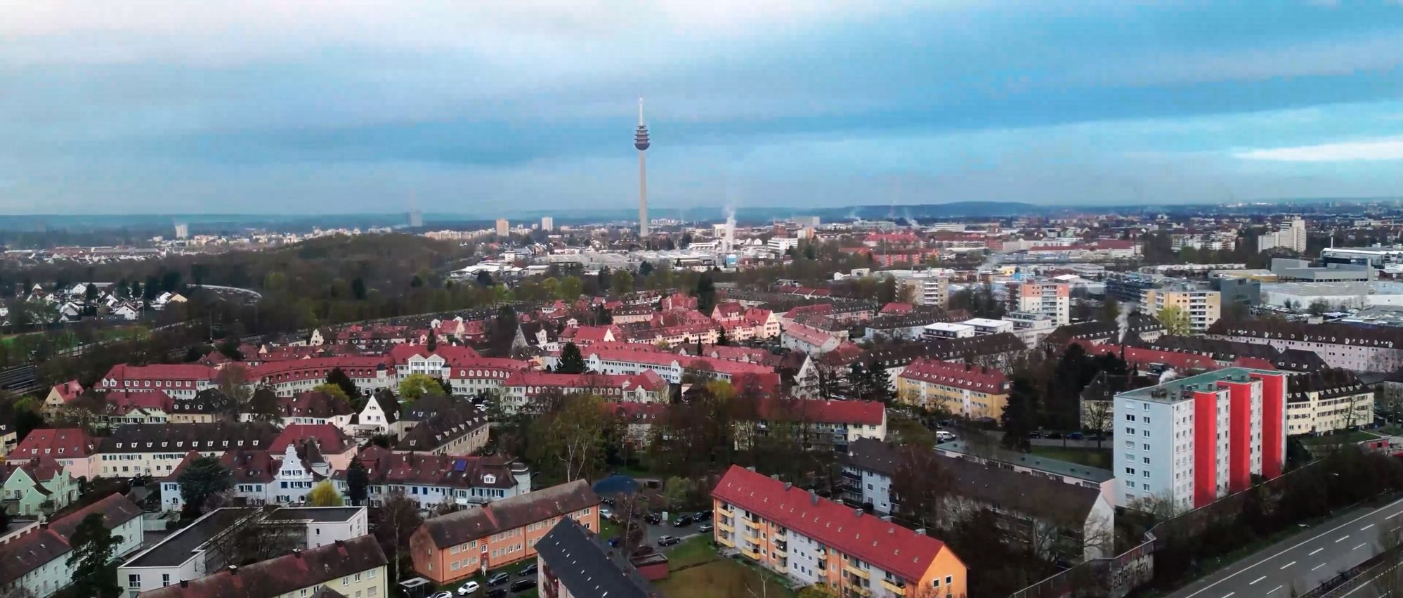 Luftaufnahme einer Stadt mit Wohngebäuden, einem Fernsehturm im Hintergrund und bewölktem Himmel