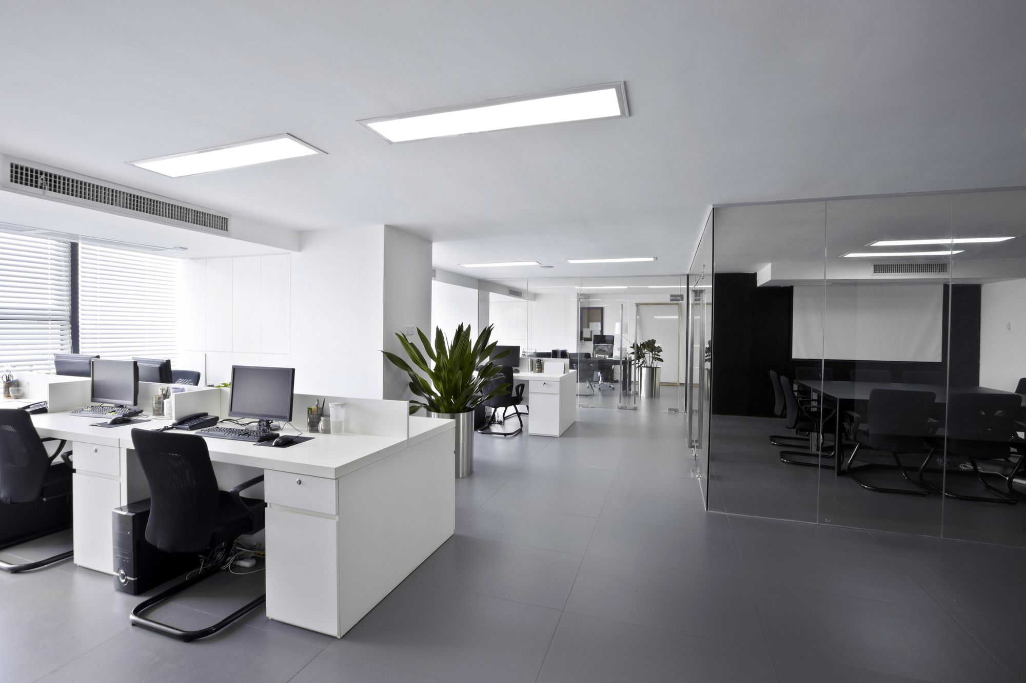 Helles Büro mit weißen Schreibtischen, Computerarbeitsplätzen, Glaswänden und Besprechungsraum
